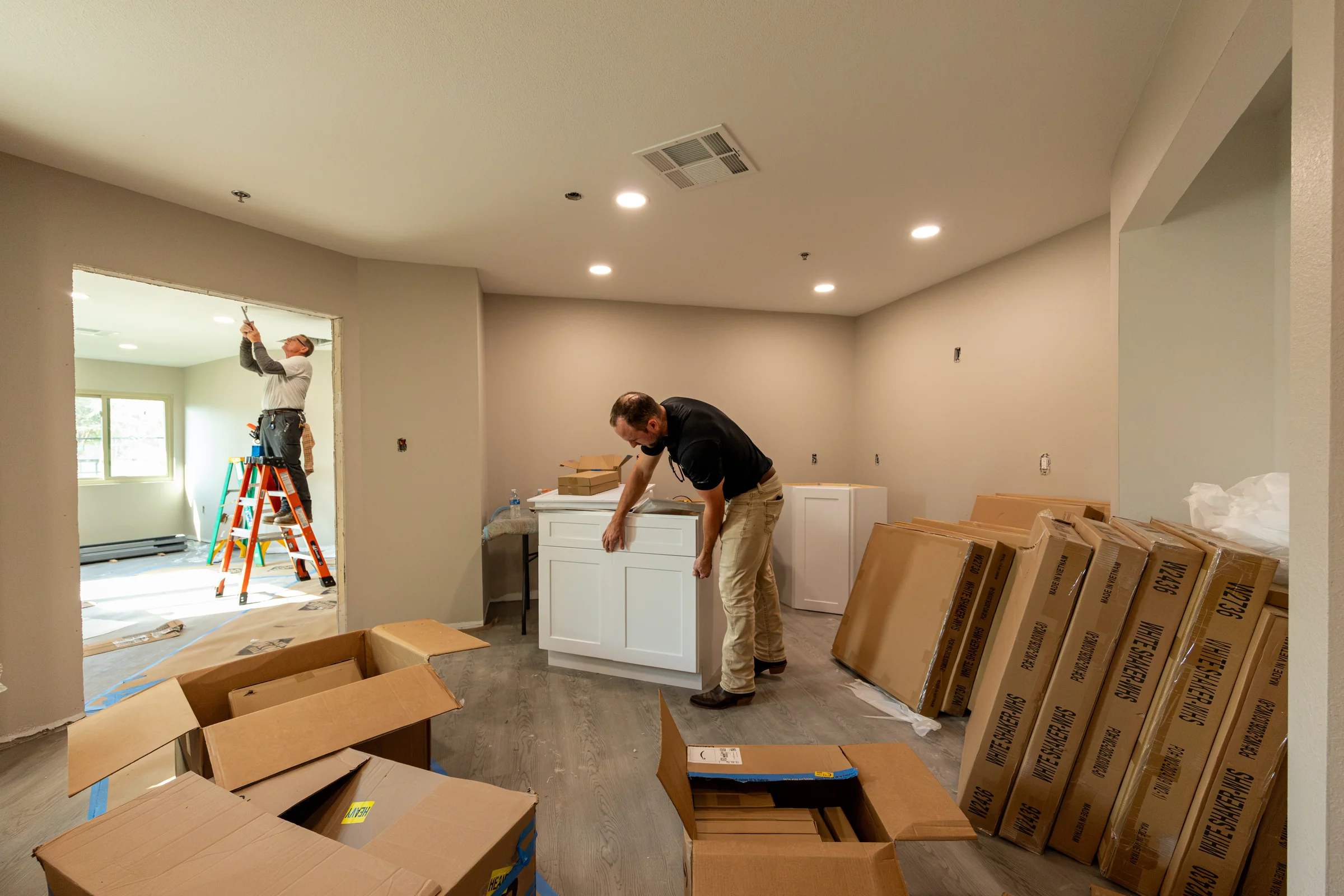 Crew members coordinating cabinetry assembly and ceiling work in one renovation area